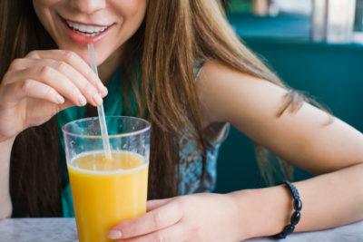 Woman drinking glass of orange juice with straw in diner