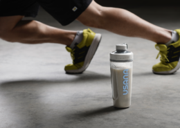 protein shake in USANA shaker bottle with a person in athletic sneakers behind it