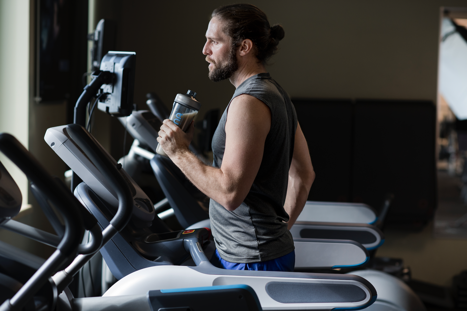 man running on treadmill in gym drinking a protein shake