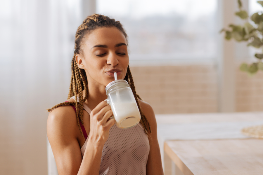 Healthy milk shake. Woman with nice hairstyle feeling good drinking healthy milk shake after working out at home