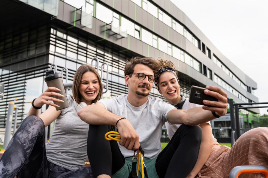 Group of people man and women male and female modern friends before or after training in sitting in open gym modern outdoor fitness park taking selfie photos with mobile phone copy space